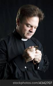 Priest holding his rosary and praying. Black background and dramatic lighting.