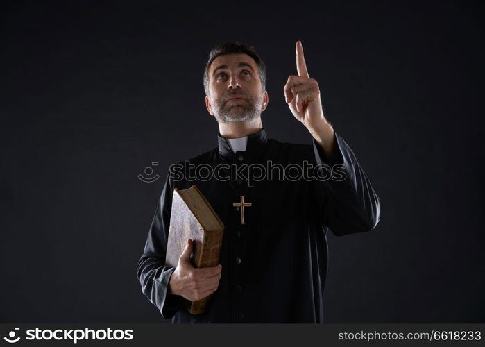 Priest male holding bible pointing finger up to heaven in sky