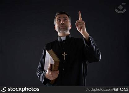 Priest male holding bible pointing finger up to heaven in sky