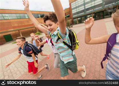 primary education and people concept - group of happy elementary school students with backpacks running and waving hands outdoors (out of focus, motion blurred image)