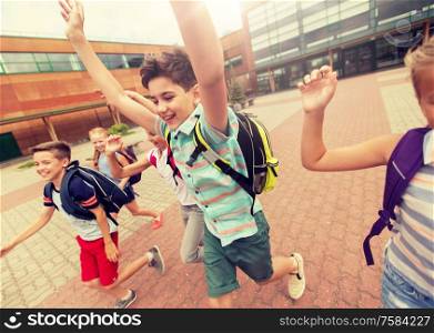 primary education and people concept - group of happy elementary school students with backpacks running and waving hands outdoors (out of focus, motion blurred image). group of happy elementary school students running