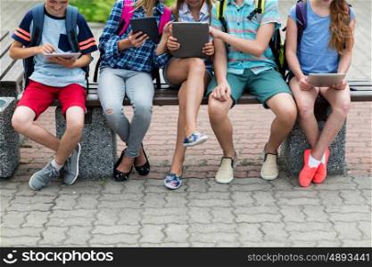 primary education, childhood, technology and people concept - close up of elementary school students with backpacks and tablet pc computers sitting on bench