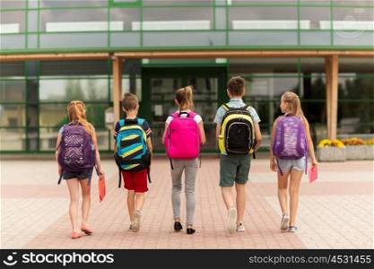 primary education, friendship, childhood and people concept - group of happy elementary school students with backpacks walking outdoors from back