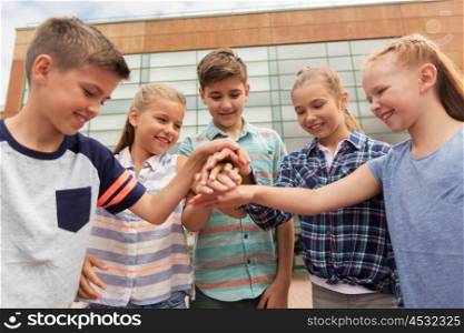 primary education, friendship, childhood and people concept - group of happy elementary school students with hands on top outdoors