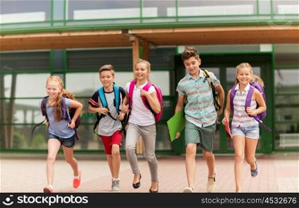 primary education, friendship, childhood and people concept - group of happy elementary school students with backpacks running outdoors