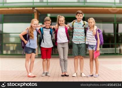 primary education, friendship, childhood and people concept - group of happy elementary school students with backpacks hugging outdoors