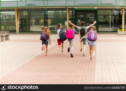 primary education, friendship, childhood and people concept - group of happy elementary school students with backpacks running outdoors