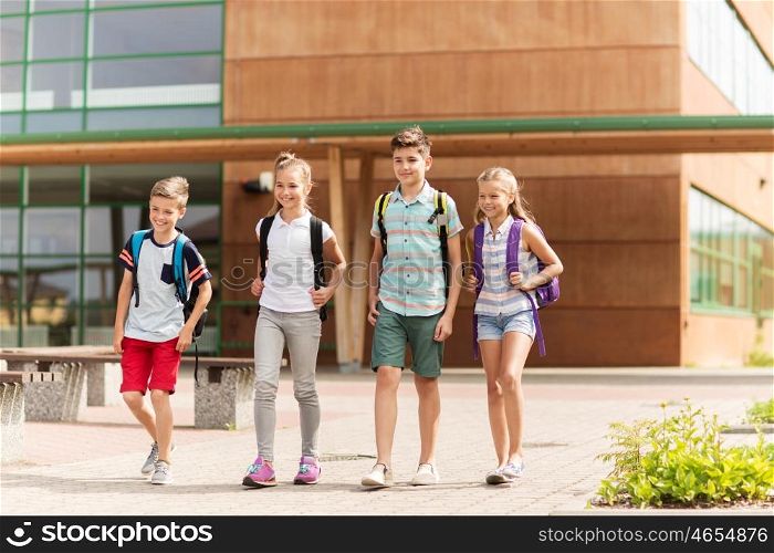 primary education, friendship, childhood and people concept - group of happy elementary school students with backpacks walking outdoors