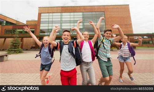 primary education, friendship, childhood and people concept - group of happy elementary school students with backpacks running and waving hands outdoors