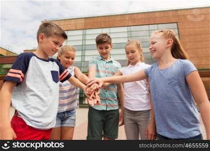 primary education, friendship, childhood and people concept - group of happy elementary school students with hands on top outdoors