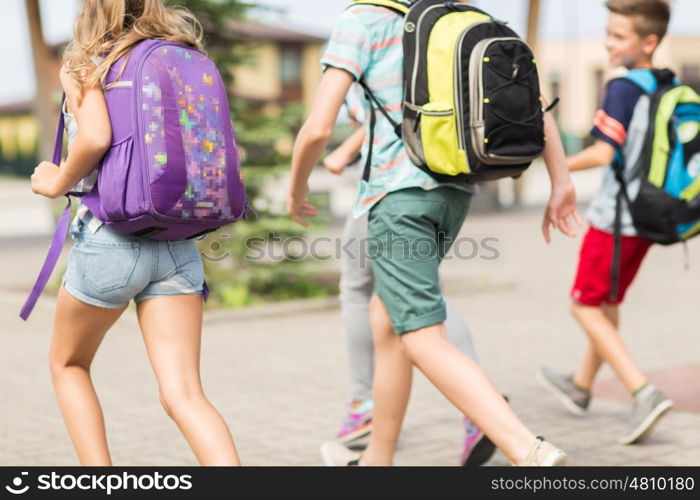 primary education, friendship, childhood and people concept - group of happy elementary school students with backpacks running outdoors