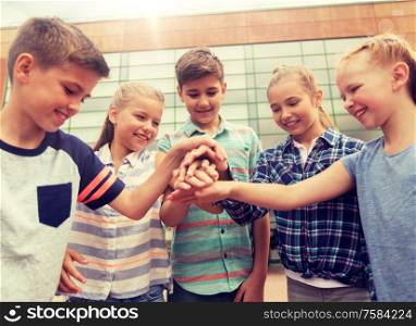 primary education, friendship, childhood and people concept - group of happy elementary school students with hands on top outdoors. group of happy elementary school students