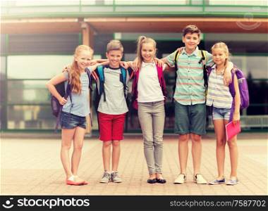 primary education, friendship, childhood and people concept - group of happy elementary school students with backpacks hugging outdoors. group of happy elementary school students hugging