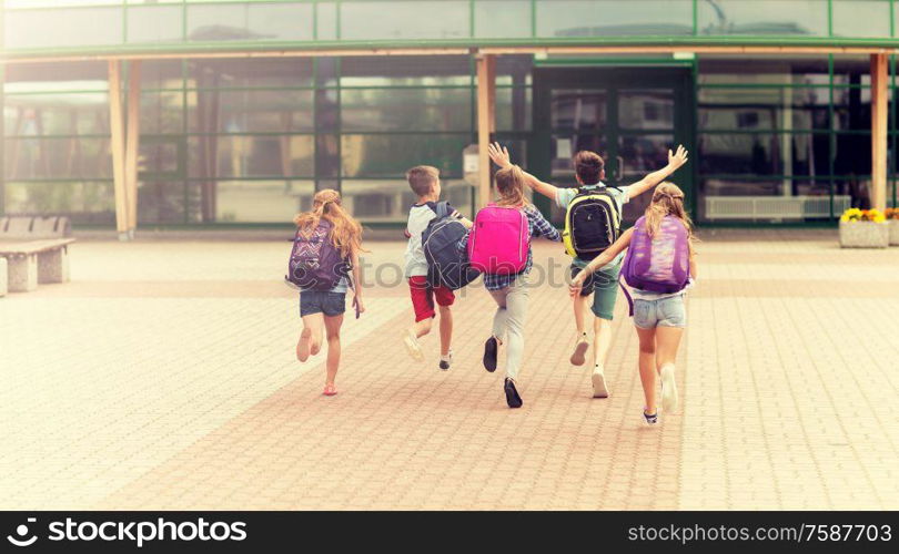 primary education, friendship, childhood and people concept - group of happy elementary school students with backpacks running outdoors. group of happy elementary school students running