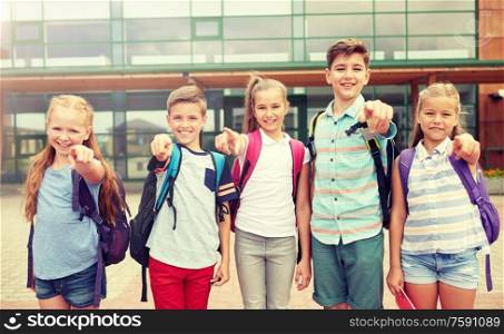primary education, friendship, childhood and people concept - group of happy elementary school students with backpacks pointing finger on you outdoors. elementary school students pointing finger on you