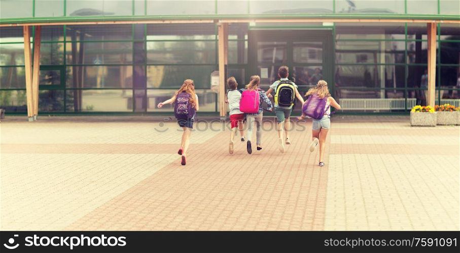 primary education, friendship, childhood and people concept - group of happy elementary school students with backpacks running outdoors. group of happy elementary school students running