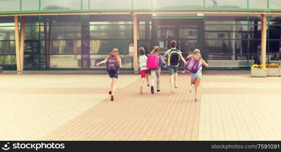 primary education, friendship, childhood and people concept - group of happy elementary school students with backpacks running outdoors. group of happy elementary school students running