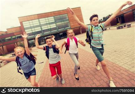 primary education, friendship, childhood and people concept - group of happy elementary school students with backpacks running and waving hands outdoors. group of happy elementary school students running