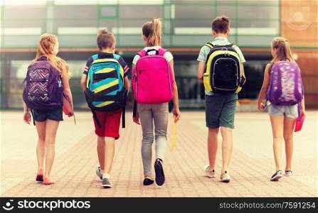 primary education, friendship, childhood and people concept - group of happy elementary school students with backpacks walking outdoors from back. group of happy elementary school students walking