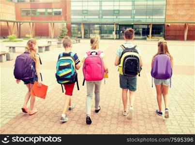 primary education, friendship, childhood and people concept - group of happy elementary school students with backpacks walking outdoors from back. group of happy elementary school students walking