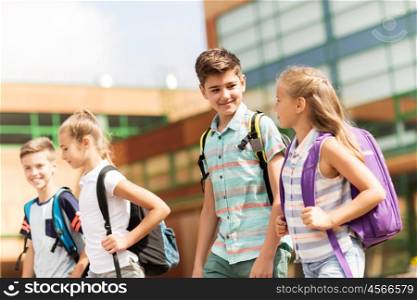primary education, friendship, childhood, communication and people concept - group of happy elementary school students with backpacks walking and talking outdoors