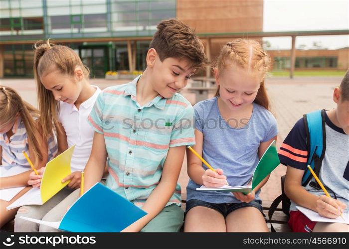 primary education, friendship, childhood, communication and people concept - group of happy elementary school students with notebooks sitting on bench outdoors