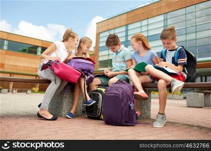 primary education, friendship, childhood, communication and people concept - group of happy elementary school students with backpacks and notebooks sitting on bench and doing homework outdoors