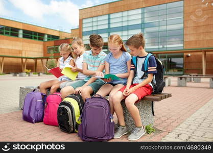 primary education, friendship, childhood, communication and people concept - group of happy elementary school students with backpacks and notebooks sitting on bench outdoors