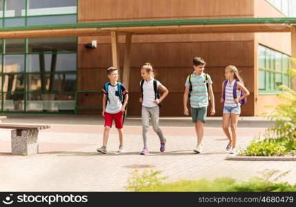 primary education, friendship, childhood, communication and people concept - group of happy elementary school students with backpacks walking and talking outdoors