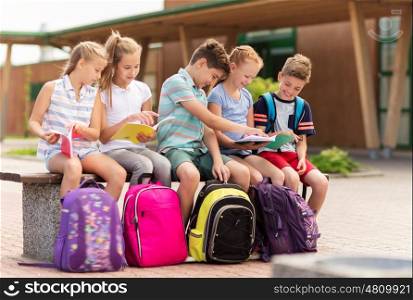 primary education, friendship, childhood, communication and people concept - group of happy elementary school students with backpacks and notebooks sitting on bench outdoors