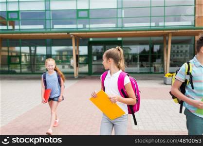 primary education, friendship, childhood, communication and people concept - group of happy elementary school students with backpacks and folders walking outdoors