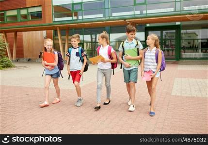 primary education, friendship, childhood, communication and people concept - group of happy elementary school students with backpacks walking and talking outdoors