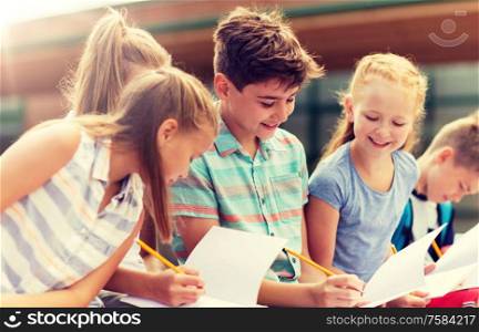 primary education, friendship, childhood, communication and people concept - group of happy elementary school students with notebooks sitting on bench outdoors. group of happy elementary school students outdoors