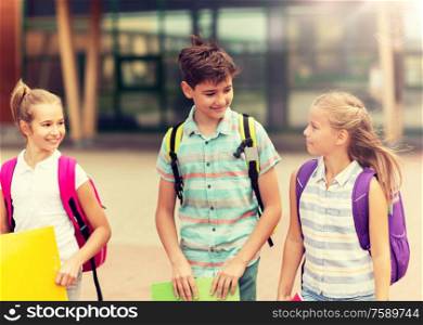 primary education, friendship, childhood, communication and people concept - group of happy elementary school students with backpacks walking and talking outdoors. group of happy elementary school students walking