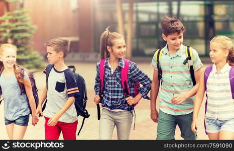 primary education, friendship, childhood, communication and people concept - group of happy elementary school students with backpacks walking and talking outdoors. group of happy elementary school students walking