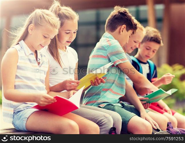 primary education, friendship, childhood, communication and people concept - group of happy elementary school students with notebooks sitting on bench outdoors. group of happy elementary school students outdoors