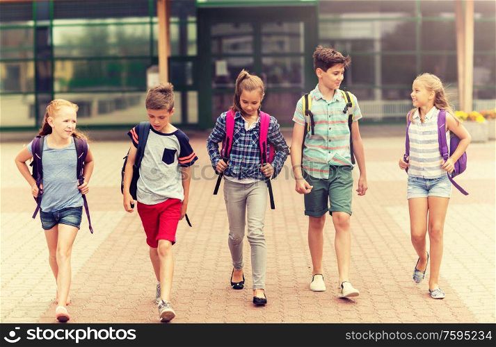 primary education, friendship, childhood, communication and people concept - group of happy elementary school students with backpacks walking and talking outdoors. group of happy elementary school students walking