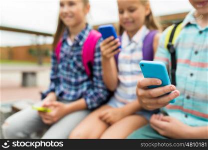 primary education, friendship, childhood, technology and people concept - group of happy elementary school students with smartphones and backpacks outdoors