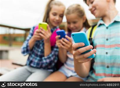 primary education, friendship, childhood, technology and people concept - group of happy elementary school students with smartphones and backpacks outdoors