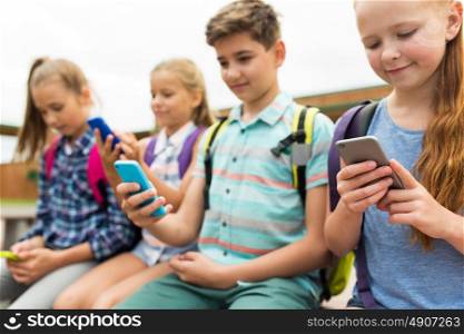 primary education, friendship, childhood, technology and people concept - group of happy elementary school students with smartphones and backpacks outdoors. elementary school students with smartphones