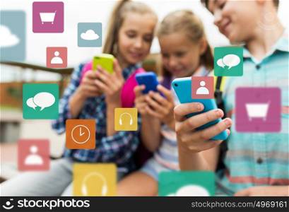 primary education, friendship, childhood, technology and people concept - group of happy elementary school students with smartphones and backpacks outdoors over multimedia icons. elementary school students with smartphones
