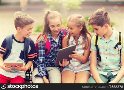 primary education, friendship, childhood, technology and people concept - group of happy elementary school students with backpacks sitting on bench and talking outdoors. group of happy elementary school students talking