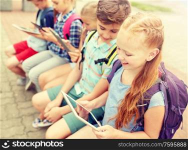 primary education, friendship, childhood, technology and people concept - group of happy elementary school students with backpacks sitting on bench and talking outdoors. group of happy elementary school students talking