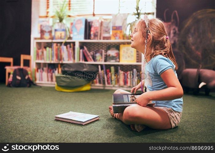 Primary schoolgirl doing homework in school library. Student learning from books. Pupil having fun studying interesting books. Back to school