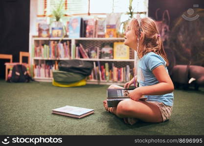 Primary schoolgirl doing homework in school library. Student learning from books. Pupil having fun studying interesting books. Back to school