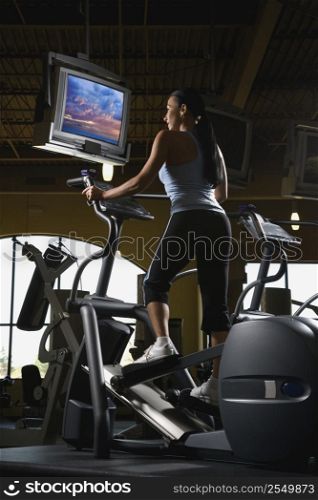 Prime adult Caucasian female on elliptical machine at gym.
