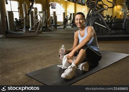 Prime adult Caucasian female sitting on mat on gym floor.