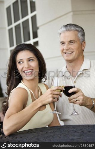 Prime adult Hispanic female and Caucasian prime adult male toasting sitting at table.