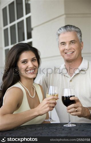 Prime adult Hispanic female and Caucasian prime adult male toasting sitting at table.