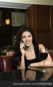 Prime adult Hispanic female sitting at bar talking on cellphone.